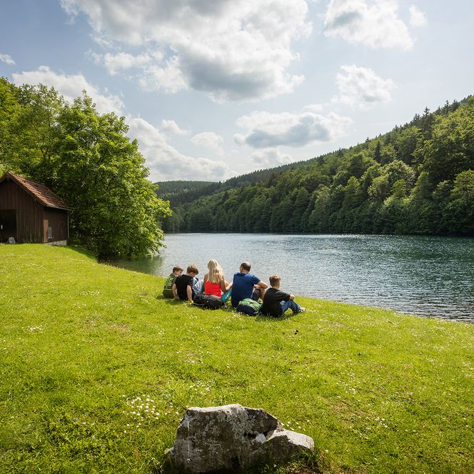 Familie sitzt auf einer Picknickdecke am See bei Brilon