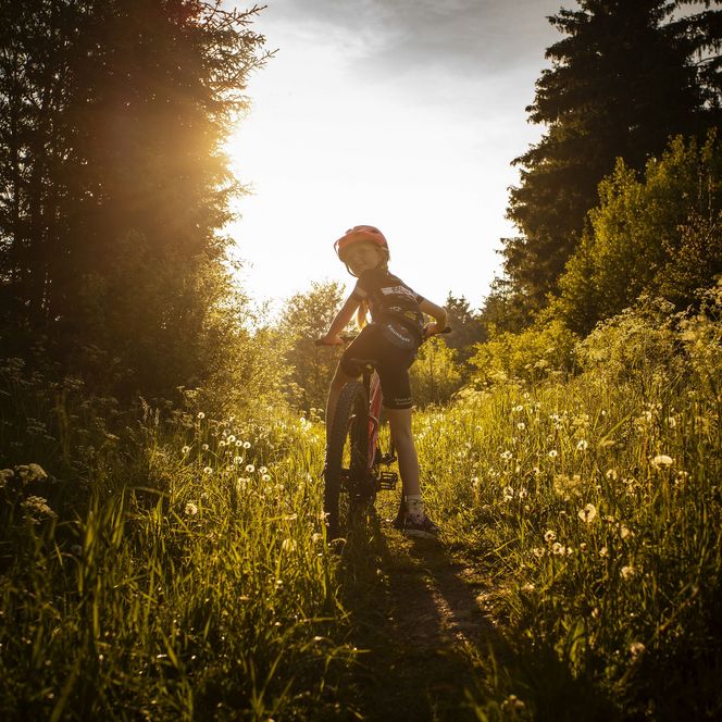 Ein Mädchen auf einem Mountainbike steht auf Wiese im Gegenlicht und dreht sich um 