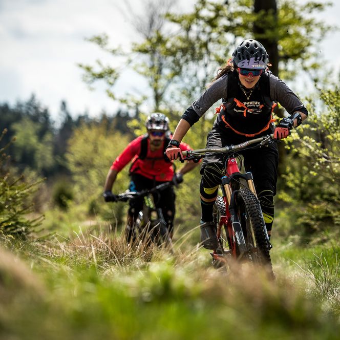 Mountainbikerin im Vordergrund und Biker fahren durch offene Landschaft über Gras in Willingen 