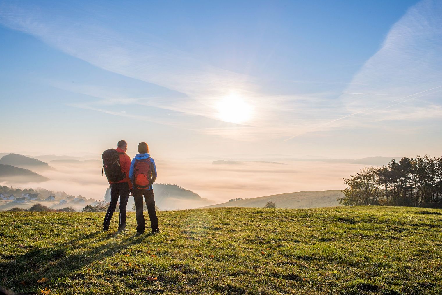 Wanderpaar bei Sonnenaufgang auf einer Wiese im Sauerland, im Tal wabert Nebel