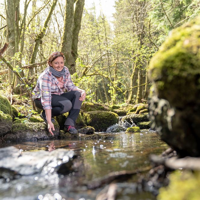 Frau in Wanderkleidung schöpft Wasser aus einem Bach
