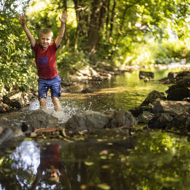 Junge planscht im Wasser eines Bachs