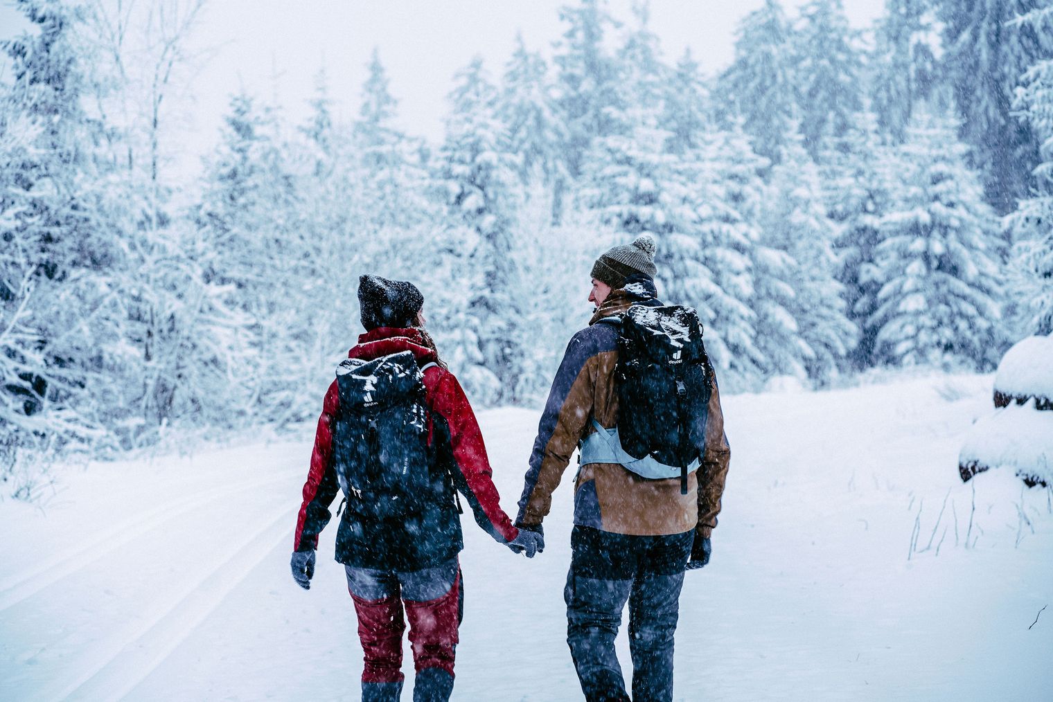 Paar wandert Hand in Hand durch verschneiten Winterwald