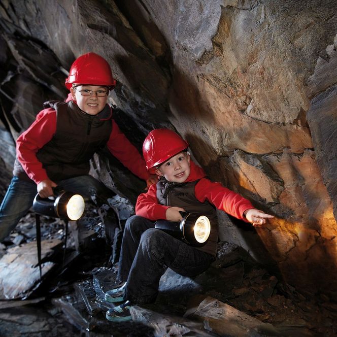 Zwei Kinder mit roten Helmen und Taschenlampen im Schieferbergwerk Willingen