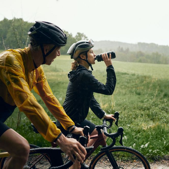 2 Gravelbiker fahren bei Regen durch eine Wiesenlandschaft im Sauerland