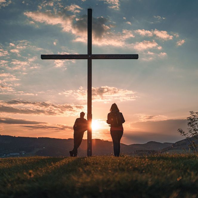 Wanderpaar beim Gipfelkreuz auf dem Orenberg bei Sonnenuntergang