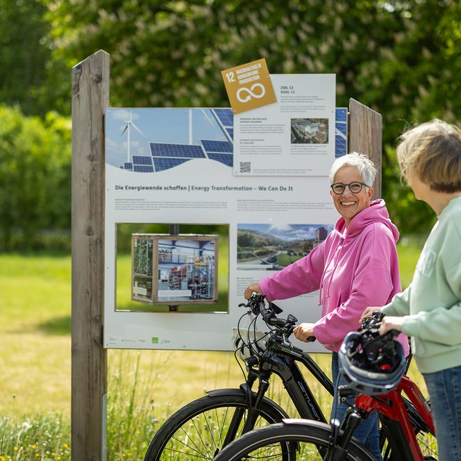 2 Bikerinnen stehen vor einer Schautafel am Radweg