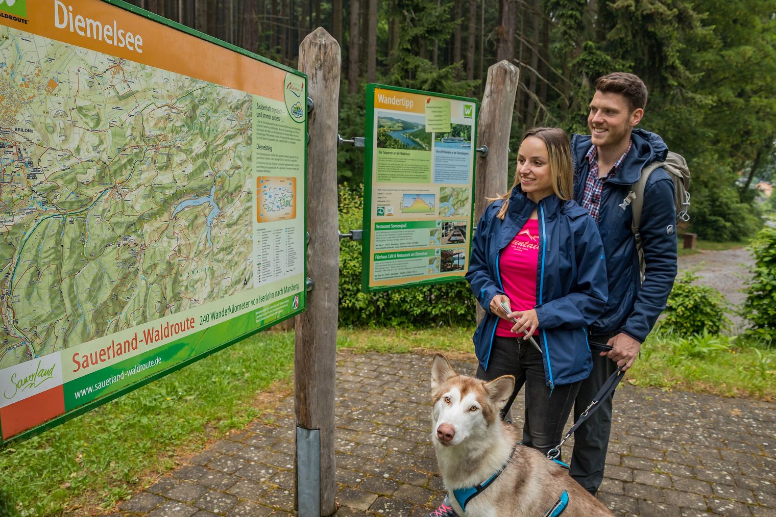 Paar mit Hund an der Wandertafel am Diemelsee