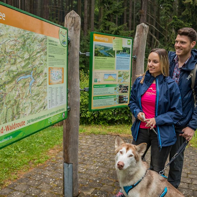 Paar mit Hund an der Wandertafel am Diemelsee